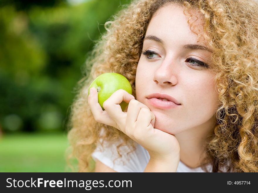 A pretty young woman outside in park holding an apple. A pretty young woman outside in park holding an apple