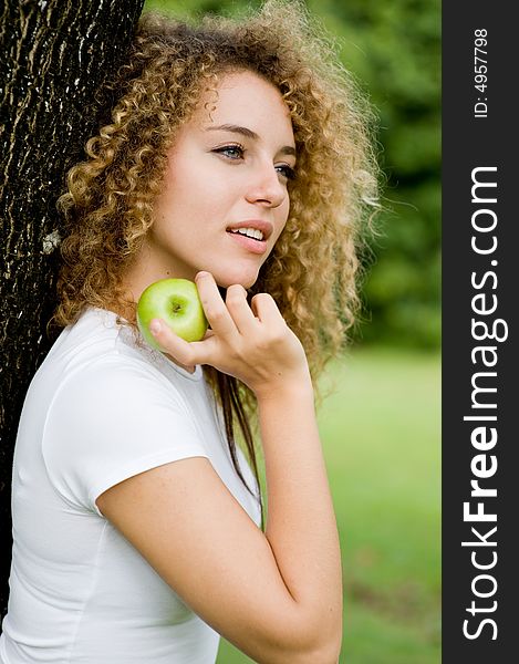 A pretty young woman outside in a park holding a green apple. A pretty young woman outside in a park holding a green apple