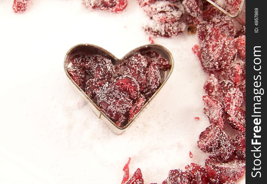 Image of dried cranberries mixed with white granulated sugar, placed in a heart-shaped cookie cutter, with other cranberries surrounding. Image of dried cranberries mixed with white granulated sugar, placed in a heart-shaped cookie cutter, with other cranberries surrounding.