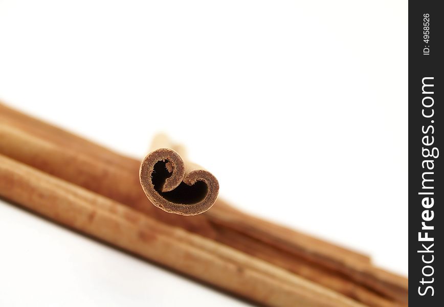 Horizontal image of piled cinnamon sticks flowing from one side of the frame to the other, with a single stick placed on top.  Curves of the single stick resemble a heart.