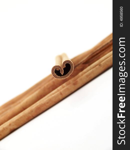 Vertical image of a pile of cinnamon sticks flowing from one side of the frame to the other, with a single stick placed on top.  Curves of the single stick resemble a heart.