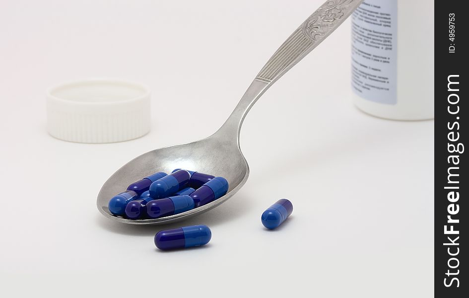 Blue pills with a spoon on a white background