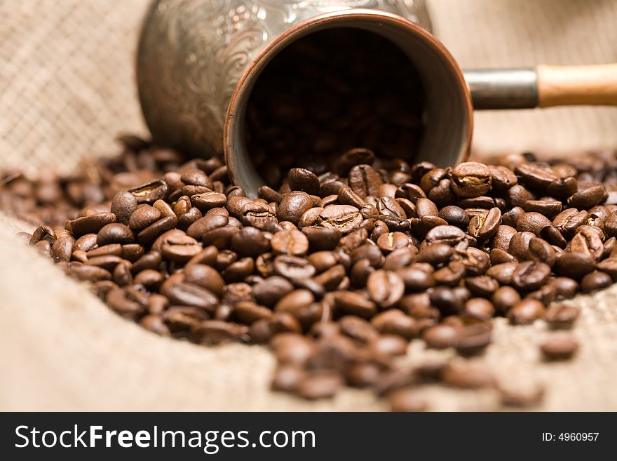 Cezve with freshly roasted coffee beans on sackcloth. Shallow depth of field. Focus on center of image