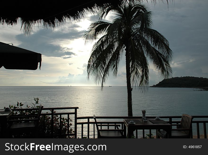 Picture of a resturant with a tropical view, trees sea and shore. Picture of a resturant with a tropical view, trees sea and shore