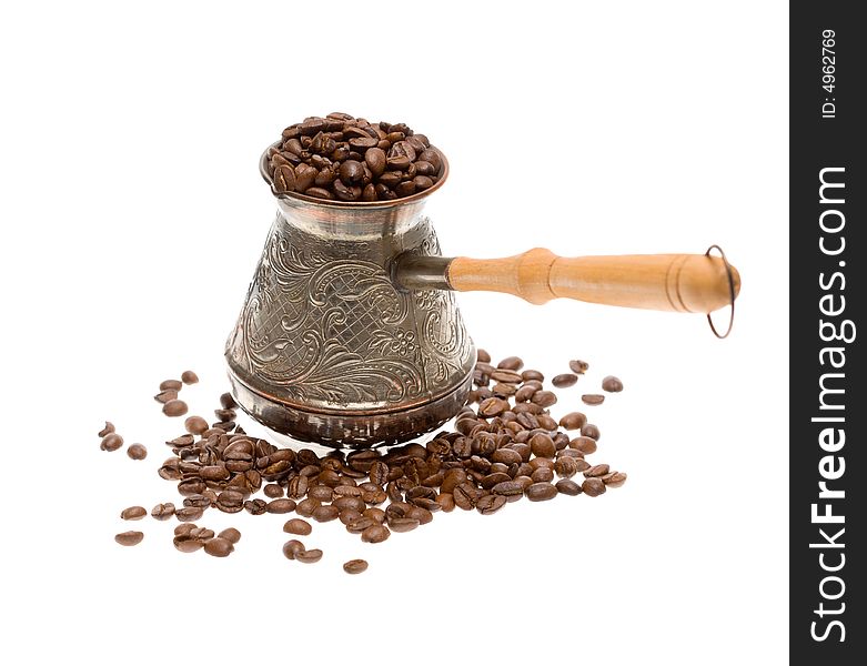 Cezve with freshly roasted coffee beans over white background. Focus on cezve. Cezve with freshly roasted coffee beans over white background. Focus on cezve