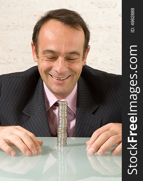 A shot of a smiling businessman looking at a stack of quarters on class desk. A shot of a smiling businessman looking at a stack of quarters on class desk.