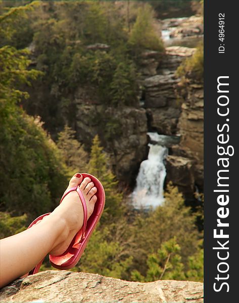 A human foot relaxing in front of a beautiful waterfall in nature. A human foot relaxing in front of a beautiful waterfall in nature.