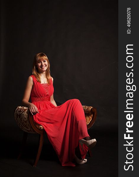 Young beautiful smiling woman in red dress sitting on a chair