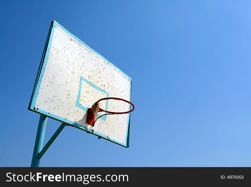 Old basketball hoop on clear blue sky.