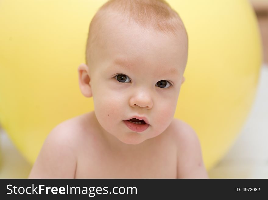 Baby with interest looking at camera against the yellow gymnastic ball