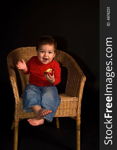 Boy sitiing in armchair, eating apple and shouting (isolated on black)