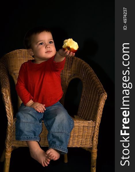 Child sitting in tha armchair and giving apple (isolated on black)