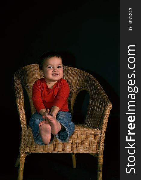 Happy boy siiting on cane-chair isolated on black