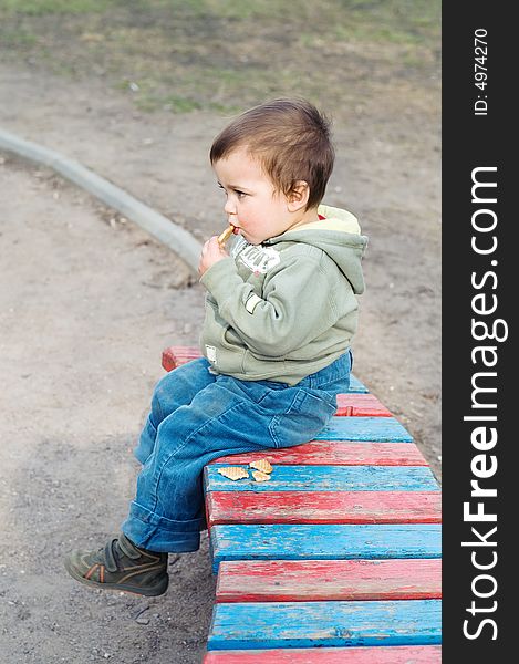 Boy eating cookie and relaxing (sitting on bench in park)