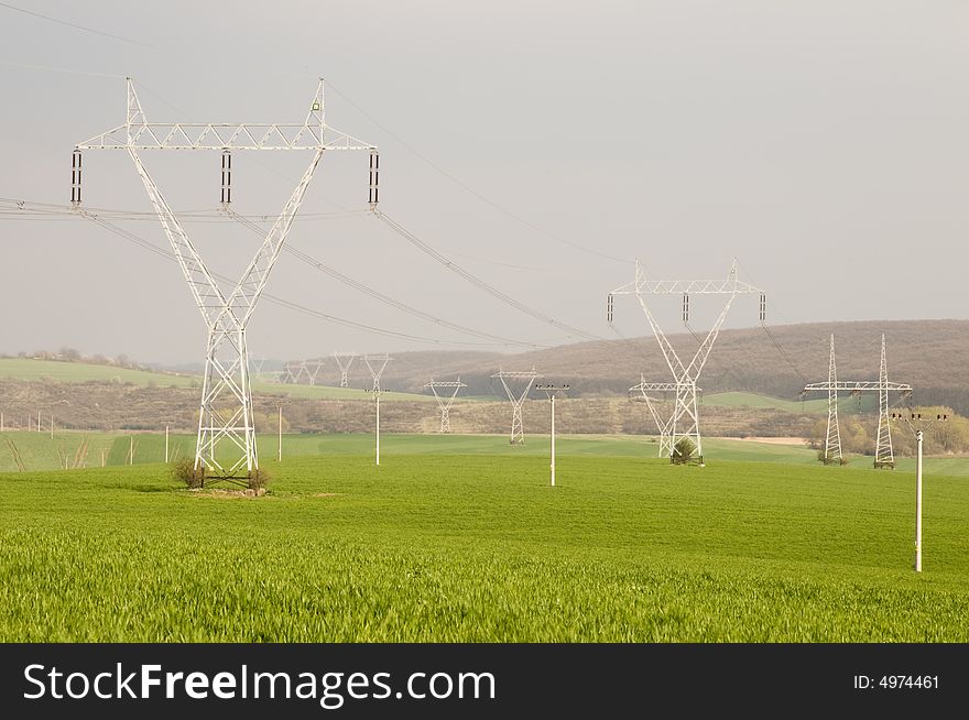 Many electricity pylons with wire in the green fields. Many electricity pylons with wire in the green fields