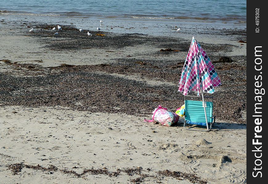A beach umbrella and chair sit alone on an empty shore. A beach umbrella and chair sit alone on an empty shore