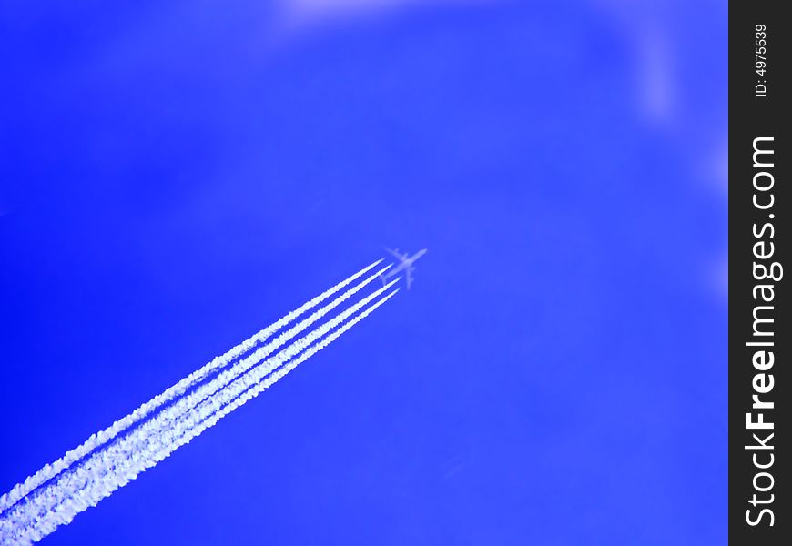 An airplane in the blue sky with white fuel tracks