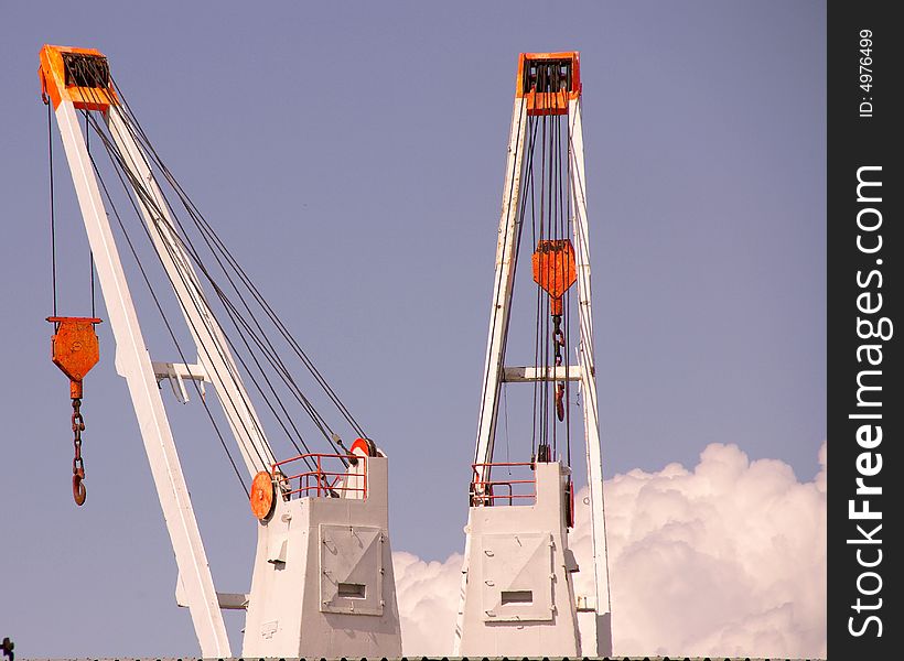 Two cranes in a trans-shipment harbour and a blue sky with one cloud