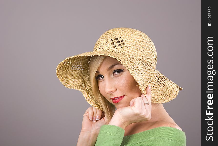 A blonde in a green blouse and a straw hat pulling the brim over her ears. A blonde in a green blouse and a straw hat pulling the brim over her ears