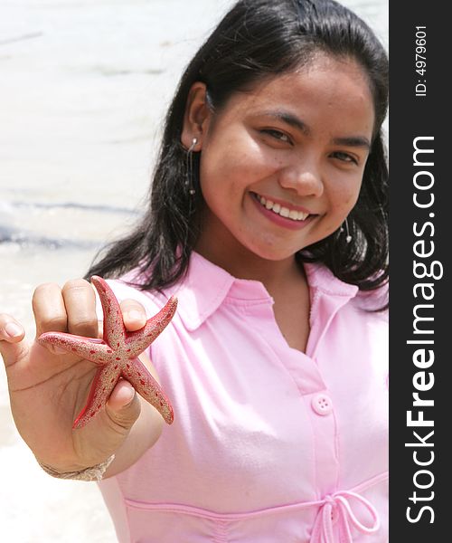 Asian girl at the beach holding up a red starfish.