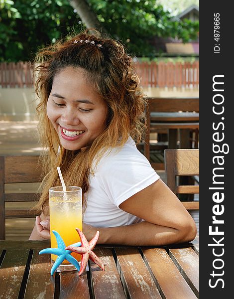 Pretty Thai woman enjoying a glass of orange juice at a cafe.