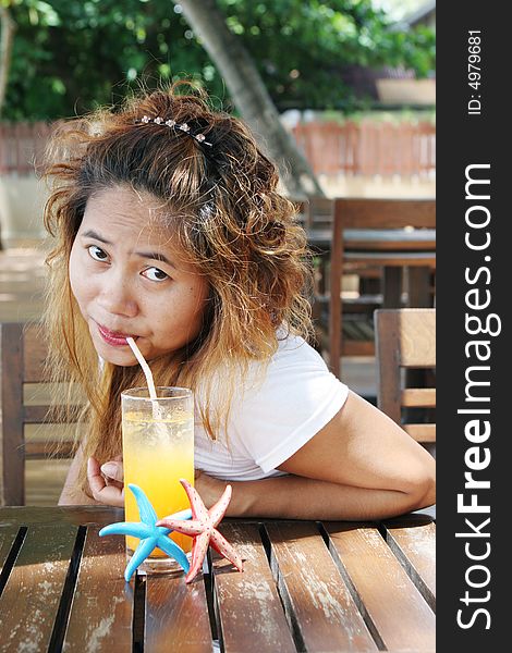 Pretty Thai woman enjoying a glass of orange juice at a cafe.