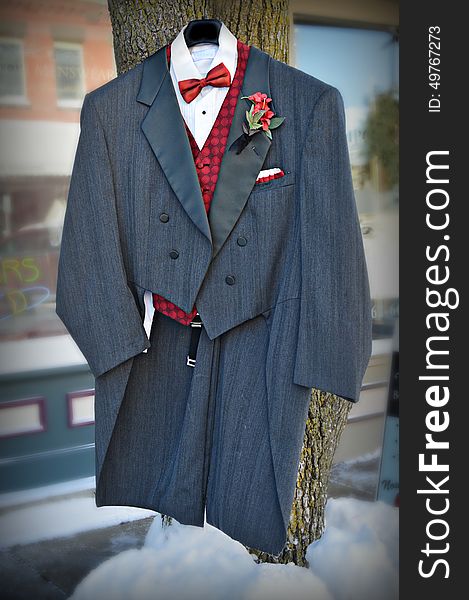 A formal Tuxedo with red vest and red bowtie and floral boutineer, hanging on a tree with snow on the ground in front of a men's formal wear store in Burlington, Wisconsin. Racine County - United States of America. A formal Tuxedo with red vest and red bowtie and floral boutineer, hanging on a tree with snow on the ground in front of a men's formal wear store in Burlington, Wisconsin. Racine County - United States of America.