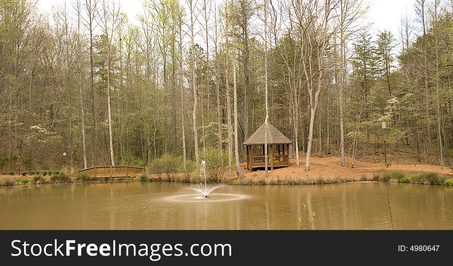 A nice wood gazebo on the shore of a lake with a fountain. A nice wood gazebo on the shore of a lake with a fountain