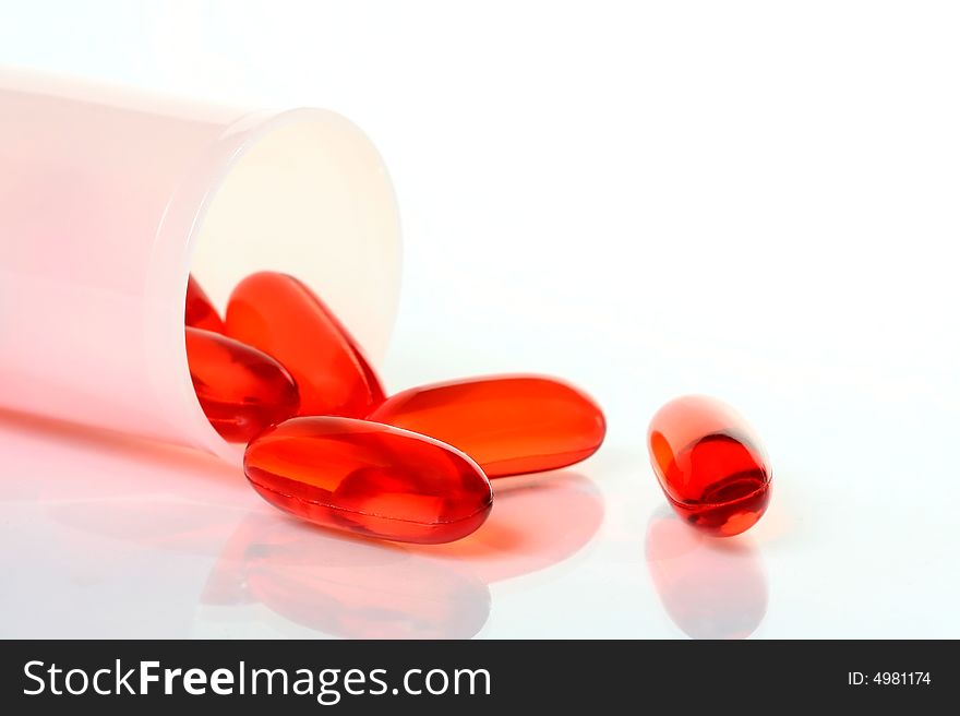 Translucent orange capsules with pill bottle on white background