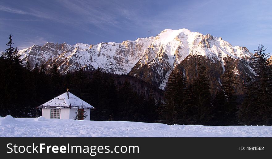 A winter landscape with a mountain peak and a small house