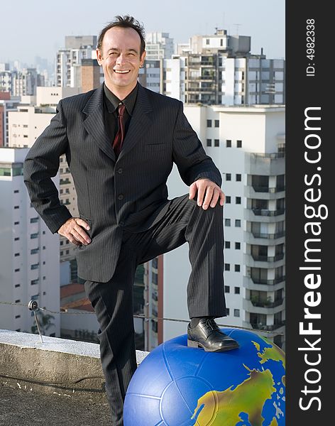 A businessman standing with one foot on the ground and the other foot on a large globe of the Earth. A businessman standing with one foot on the ground and the other foot on a large globe of the Earth.