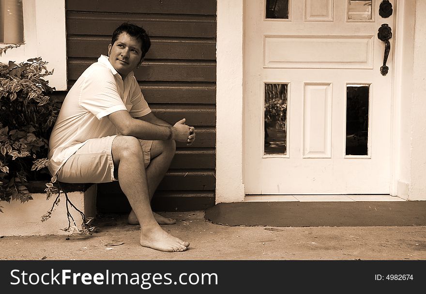 Black and white of a man sitting next to a doorway with tropical island type architecture. Black and white of a man sitting next to a doorway with tropical island type architecture