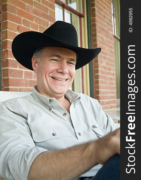 A man wearing a cowboy hat, sitting on a porch, with gentle laughter covering his face. A man wearing a cowboy hat, sitting on a porch, with gentle laughter covering his face.
