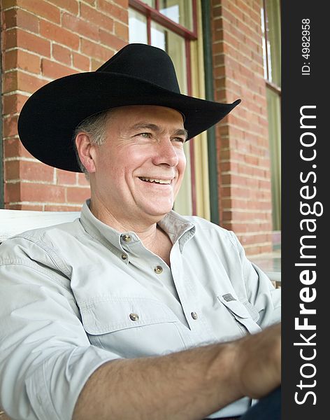 A man sitting on a porch wearing a cowboy hat with a big happy smile on his face. A man sitting on a porch wearing a cowboy hat with a big happy smile on his face.