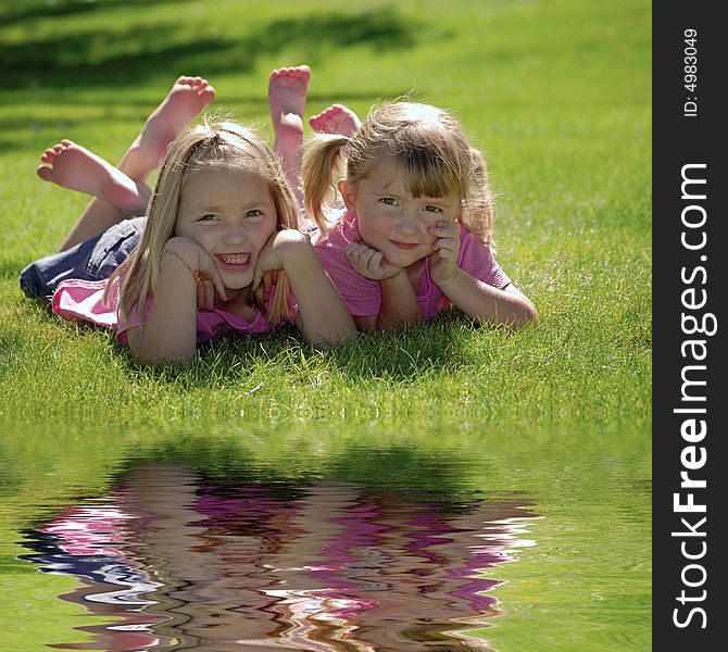Two sisters in pink shirts resting their heads on their hands by a pond. Two sisters in pink shirts resting their heads on their hands by a pond