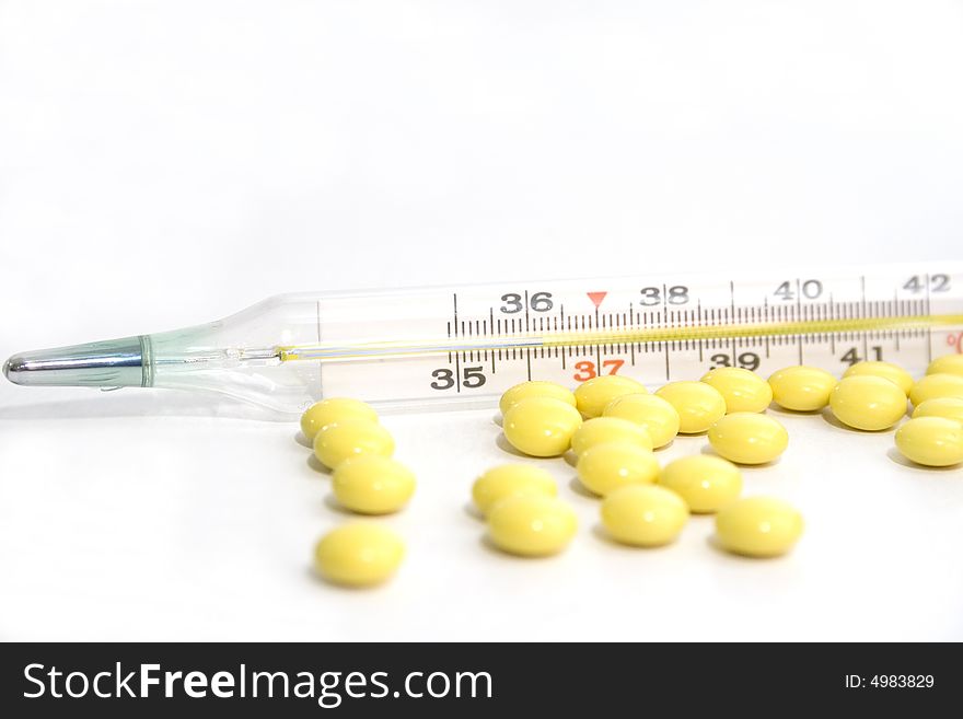 Thermometer and yellow tablets on the white background. Thermometer and yellow tablets on the white background
