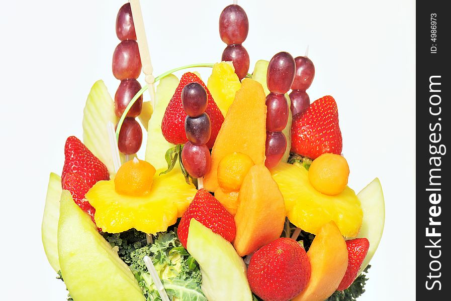 A closeup view of a colorful display and arrangement of fruit including strawberries, pineapple, melons, and grapes on sticks and embedded in lettuce. A closeup view of a colorful display and arrangement of fruit including strawberries, pineapple, melons, and grapes on sticks and embedded in lettuce.