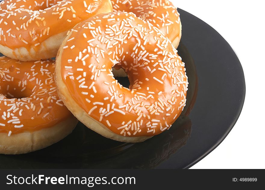 Orange glazed donuts with white sprinkles on a black plate isolated on a white background. Orange glazed donuts with white sprinkles on a black plate isolated on a white background.