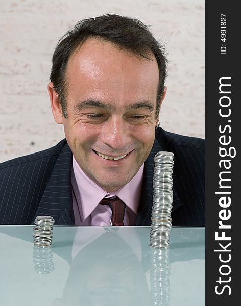 Business man in a suit and tie with two uneven stacks of coins in front of him. Business man in a suit and tie with two uneven stacks of coins in front of him