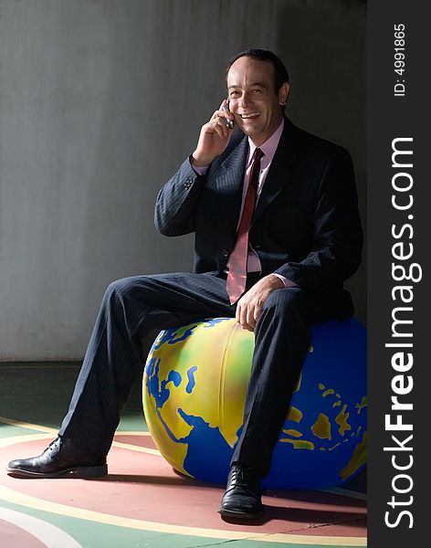 A shot of businessman sitting on globe talking on cellphone. A shot of businessman sitting on globe talking on cellphone.