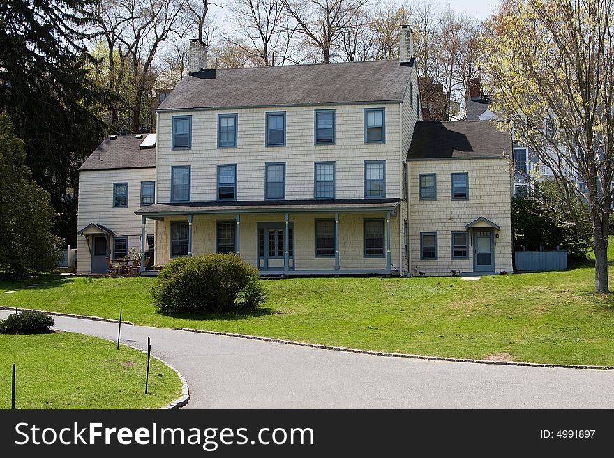 A remotely located white Victorian/Colonial mansion in the woods on a spring day.