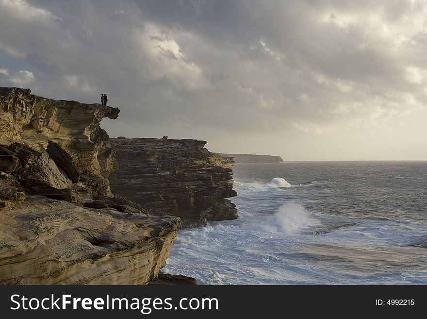 Wild ocean and two people silhouettes standing at the top of he limestone cliffs. Wild ocean and two people silhouettes standing at the top of he limestone cliffs