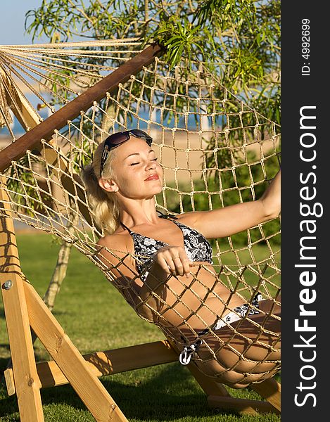 White model lies in the hammock on a background of green branch on the beach. White model lies in the hammock on a background of green branch on the beach.