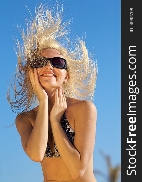 Posing young woman with blond long hair and happy smiling facial expression on a blue (sky) background. In Marilyn Monroe style.