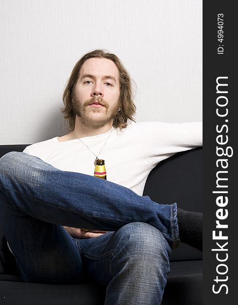 Young man with bottle of beer sitting on the sofa