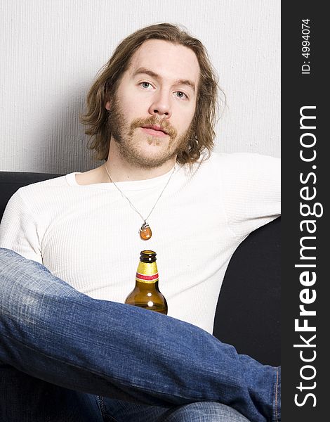 Young man with bottle of beer sitting on the sofa