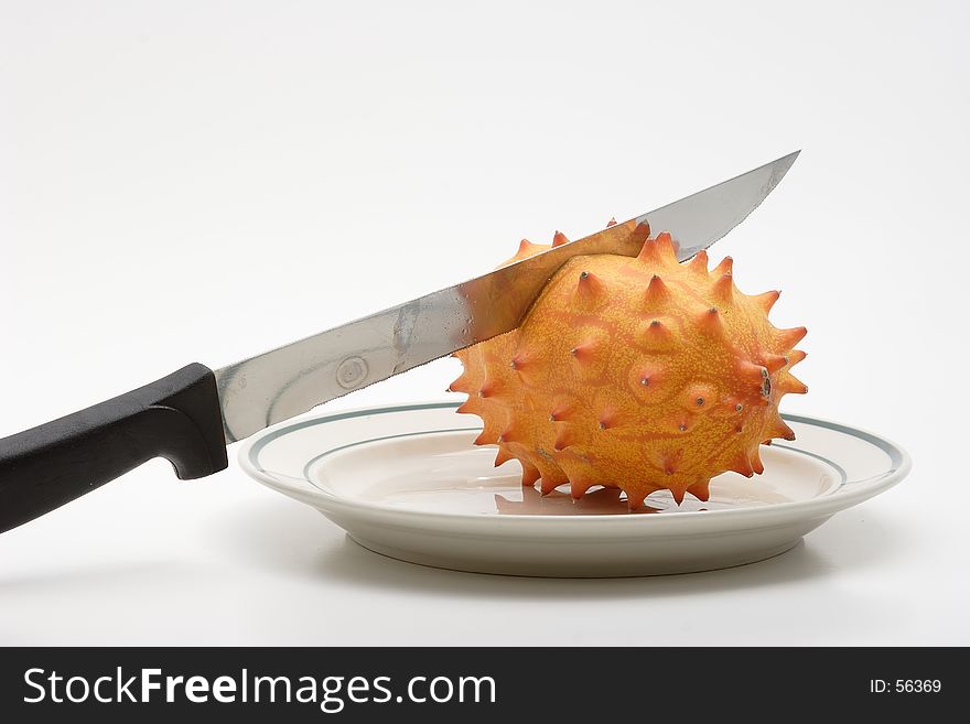 A knife beginning to slice a kiwiano fruit. A knife beginning to slice a kiwiano fruit