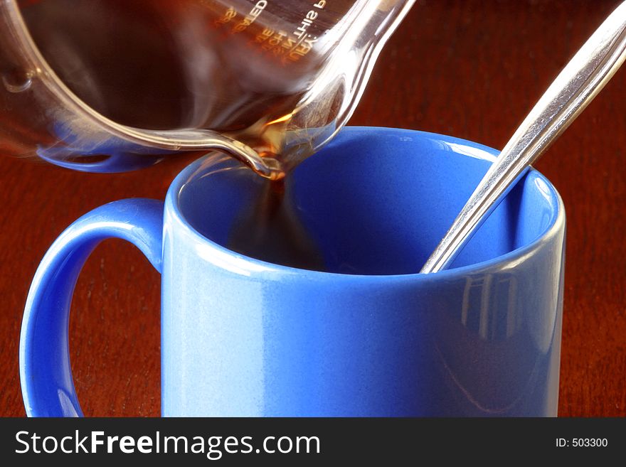 A pot of hot steaming coffee being poured into a blue cup with a silver spoon in it. A cherry wood table is the background. A moring or awake all night concept Coffee caffeine pick-me-up drink mug table aroma black coffee beginnings pure delicious american culture strong & dark HOT Steaming food and beverage photo illustration colorful. A pot of hot steaming coffee being poured into a blue cup with a silver spoon in it. A cherry wood table is the background. A moring or awake all night concept Coffee caffeine pick-me-up drink mug table aroma black coffee beginnings pure delicious american culture strong & dark HOT Steaming food and beverage photo illustration colorful