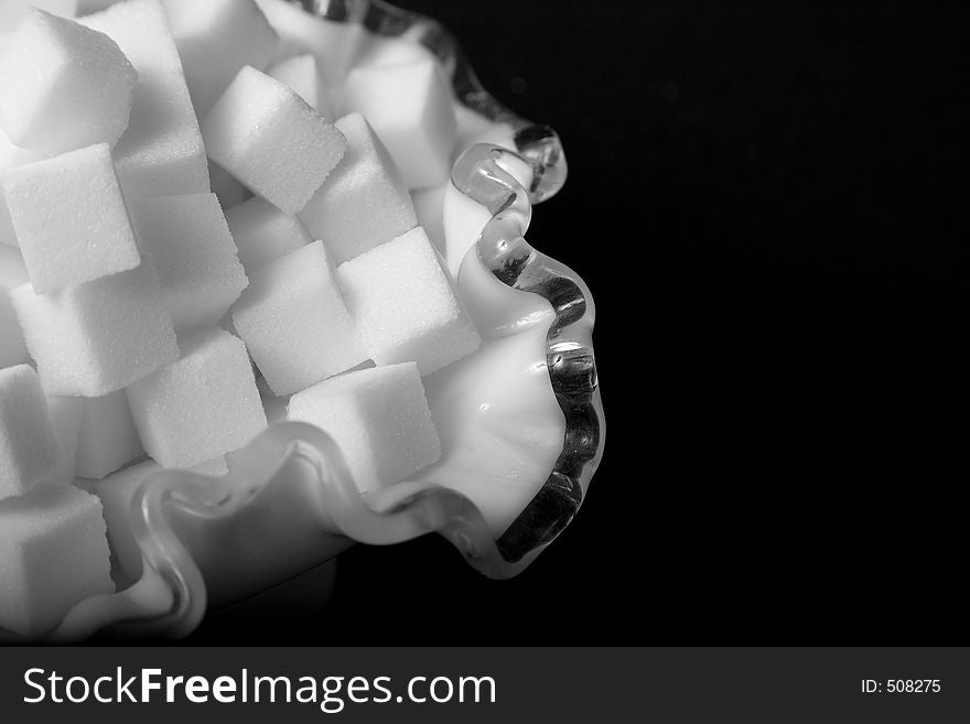Macro of sugar cubes in frilly glass bowl against black. Macro of sugar cubes in frilly glass bowl against black