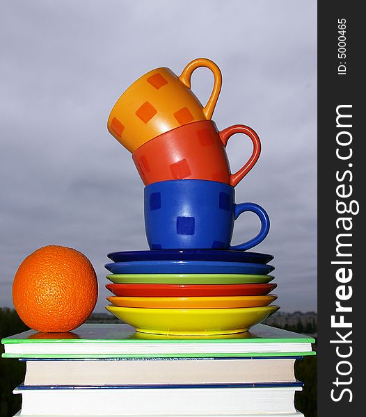 Multi-colored cups, books and ripe orange. Multi-colored cups, books and ripe orange